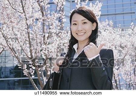 Stock Photography - Young woman in suit standing in front of cherry blossoms. Fotosearch