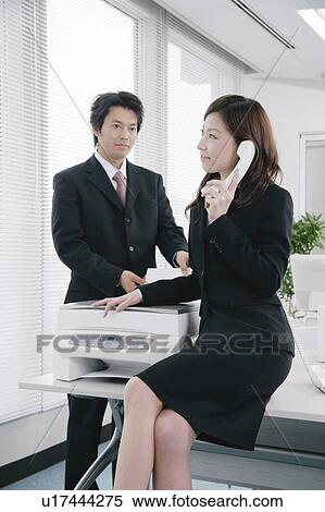 Stock Photography - Young woman talking over phone sitting on desk. Fotosearch