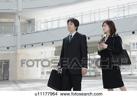 Picture - A mid adult businessman and young businesswoman walking. Fotosearch