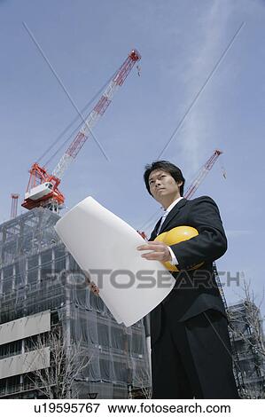 Stock Photo - A mid adult businessman standing at construction site. Fotosearch