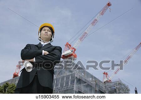 Stock Photography - A mid adult businessman standing at construction site. Fotosearch