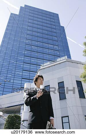 Stock Photograph - A mid adult businessman standing with a mobile phone. Fotosearch