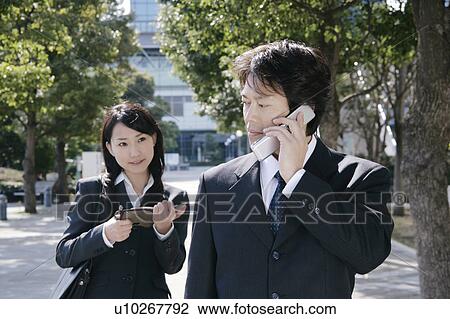 A mid adult businessman talking over mobile phone and young businesswoman standing behind View Large Photo Image Stock Image - A mid adult businessman talking over mobile phone and young businesswoman standing behind. Fotosearch