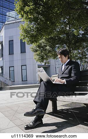 A mid adult businessman using PC sitting on bench View Large Photo Image Stock Photo - A mid adult businessman using PC sitting on bench. Fotosearch