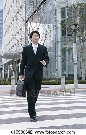 Stock Image - A mid adult businessman walking on zebra crossing. Fotosearch