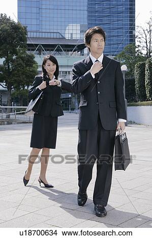 Picture - A mid adult man adjusting tie and a young woman standing behind. Fotosearch