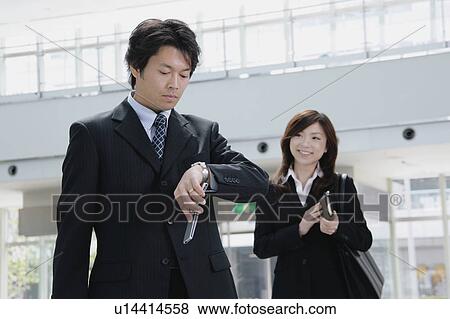 A mid adult man looking at watch and a young woman standing behind View Large Photo Image Stock Photo - A mid adult man looking at watch and a young woman standing behind. Fotosearch