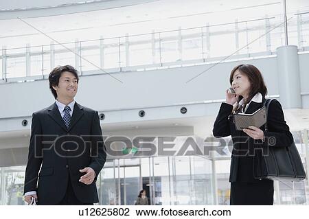 A young businesswoman talking over mobile phone and her boss standing aside View Large Photo Image Stock Image - A young businesswoman talking over mobile phone and her boss standing aside. Fotosearch