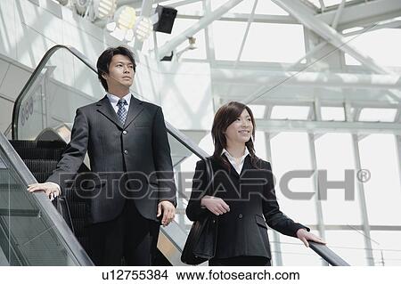 Picture - A young woman and a mid adult man moving down escalator. Fotosearch