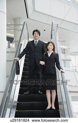 A young woman and a mid adult man moving down escalator View Large Photo Image Picture - A young woman and a mid adult man moving down escalator. Fotosearch