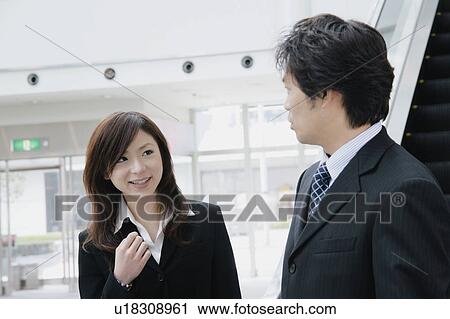 Stock Image - A young woman and a mid adult man talking in front of escalator. Fotosearch