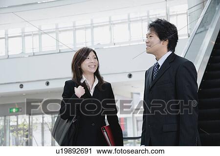 Stock Image - A young woman and a mid adult man talking in front of escalator. Fotosearch