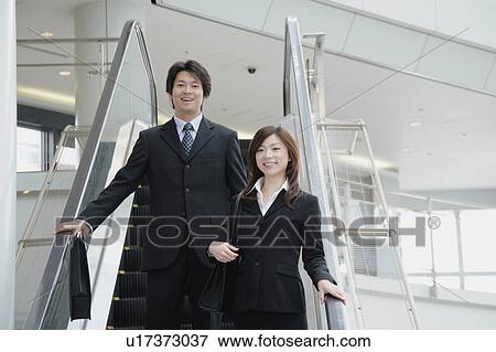 Stock Photo - A young woman and a mid adult man moving down escalator. Fotosearch