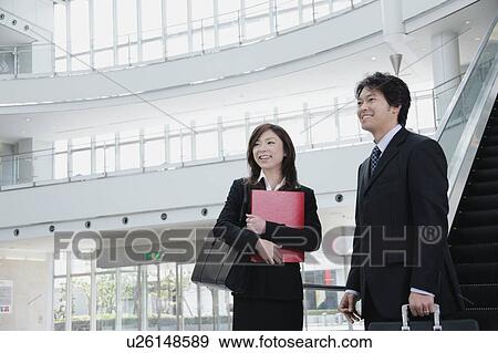 Stock Photo - A young woman and a mid adult man standing in front of escalator. Fotosearch