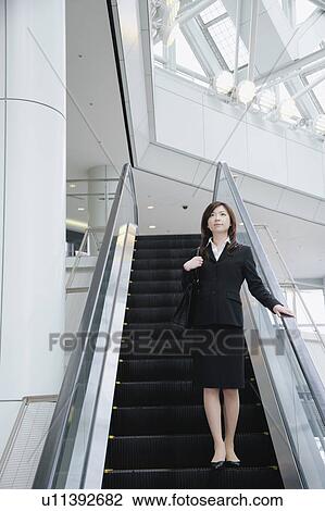 Stock Image - A young woman in suit going down escalator. Fotosearch