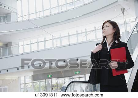 Stock Image - A young woman in suit going down escalator. Fotosearch