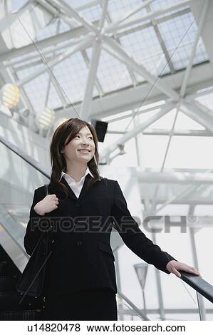 Stock Photo - A young woman in suit going down escalator. Fotosearch