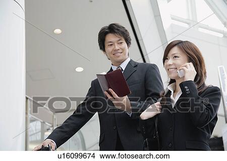A young woman talking over mobile phone and a mid adult man standing with personal organizer View Large Photo Image Picture - A young woman talking over mobile phone and a mid adult man standing with personal organizer. Fotosearch