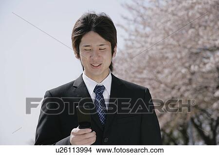 Picture - A young man in suit looking at mobile phone. Fotosearch