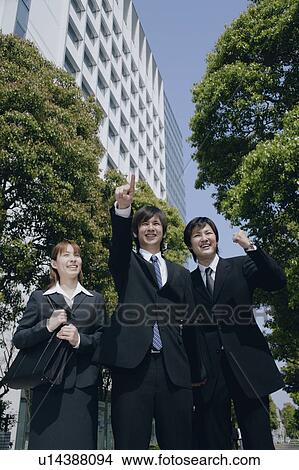 Picture - A young man in suit pointing ahead with his friends standing aside. Fotosearch