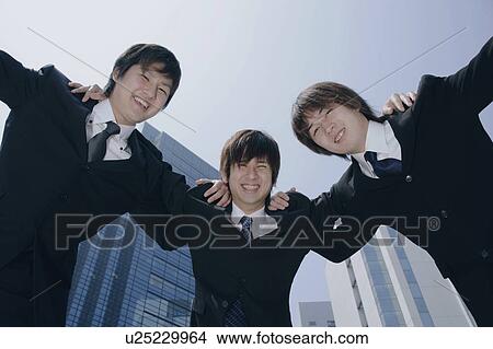 Picture - Three young men in suit huddling. Fotosearch