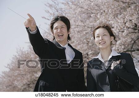 Stock Photography - Young man in suit pointing ahead and a young woman standing aside. Fotosearch