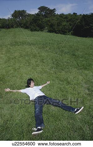 Stock Image - A young man lying on grass with his arms and legs widely open. Fotosearch