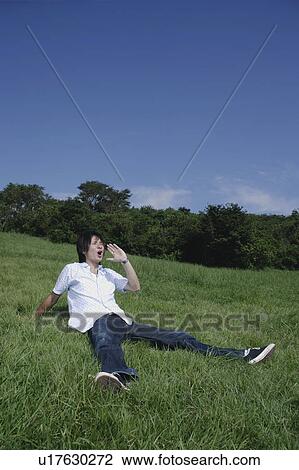 Stock Image - A young man sitting on grass and yelling. Fotosearch
