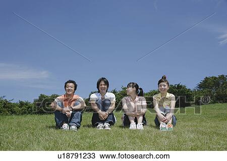 Stock Image - Four young people sitting on grass field. Fotosearch