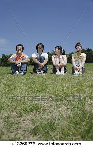 Stock Photograph - Four young people sitting on grass field. Fotosearch