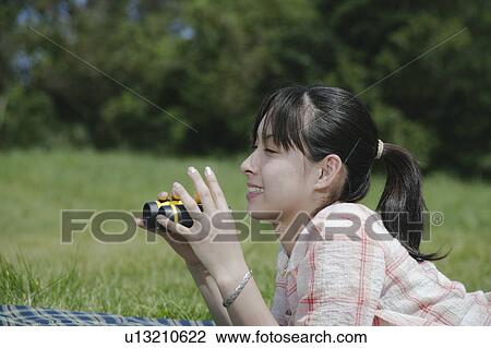 Stock Image - Young woman lying with binoculars. Fotosearch