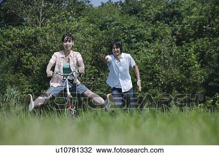Stock Image - Young woman riding on bicycle and a man following. Fotosearch