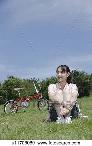 Stock Photo - Young woman sitting on grass field. Fotosearch