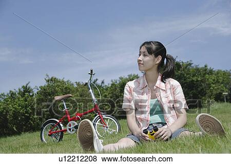 Stock Photo - Young woman sitting on grass field. Fotosearch