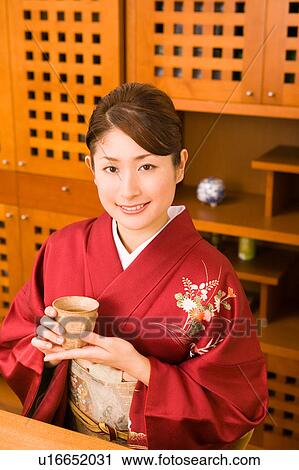 A young woman wearing kimono holding a cup of tea View Large Photo Image Stock Image - A young woman wearing kimono holding a cup of tea. Fotosearch