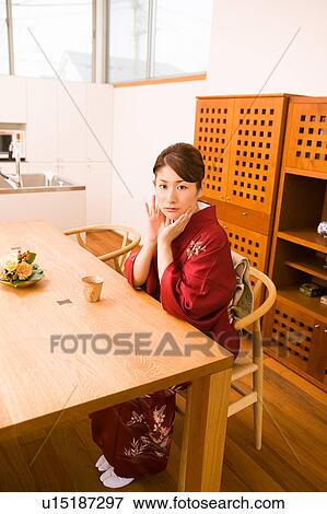 Stock Photo - A young woman wearing kimono sitting in dining room. Fotosearch