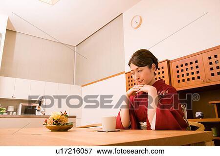 Stock Photo - A young woman wearing kimono sitting in dining room. Fotosearch