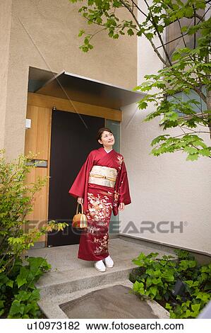 Stock Image - A young woman wearing kimono standing in front of door. Fotosearch