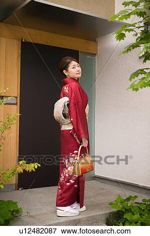 Stock Photo - A young woman wearing kimono standing in front of door. Fotosearch