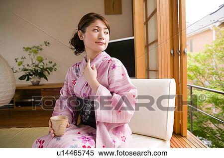 Stock Photography - A young woman wearing yukata sitting on sofa. Fotosearch