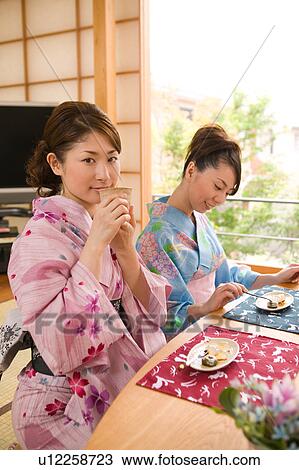 Stock Image - Two young women wearing yukata eating dessert. Fotosearch