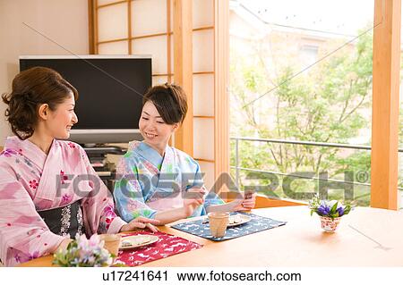 Stock Image - Two young women wearing yukata talking. Fotosearch