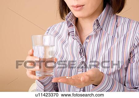 Stock Image - A woman holding glass of water and pills. Fotosearch