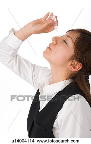 Picture - A young woman applying eye drop. Fotosearch