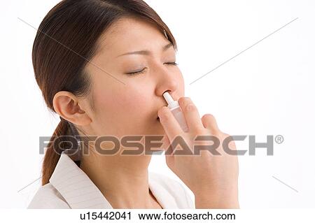 Stock Image - A young woman using nasal spray. Fotosearch