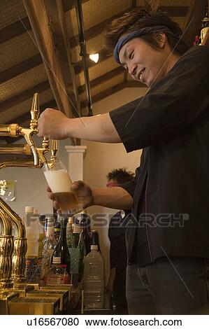 Stock Image - Bartender pouring beer to glass. Fotosearch