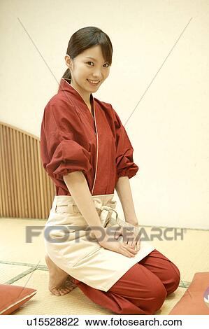 Stock Image - Portrait of young waitress sitting at Japanese restaurant. Fotosearch