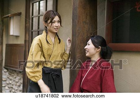 Stock Image - Two young women talking in front of restaurant. Fotosearch