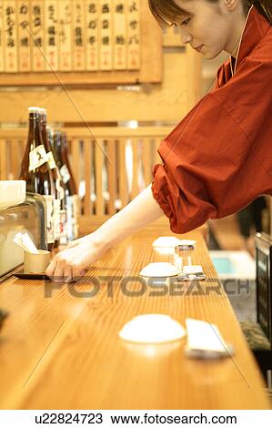 Stock Image - Waitress setting table at Japanese restaurant. Fotosearch