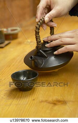 Stock Image - Woman pouring tea to tea cup. Fotosearch